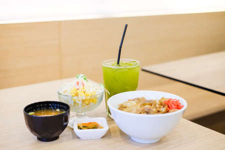 The food set consists of rice with grilled pork teriyaki, spring onion & carrot on top white bowl serve with tofu soup (Miso soup), tomato, cabbage & corn salad and green tea - japanese food concept.の写真素材