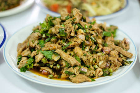 Homemade hot and spicy sliced grilled pork salad (Nam Tok Moo) serve on white plate for food background or texture - Thailand.の写真素材