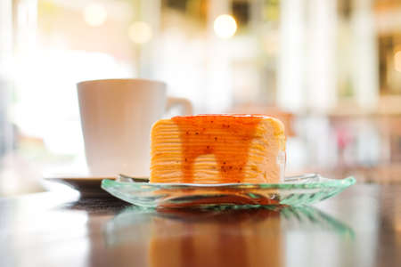 Part of crepe cake topped with strawberry sauce serve on clear dish and hot fresh milk in glass for...