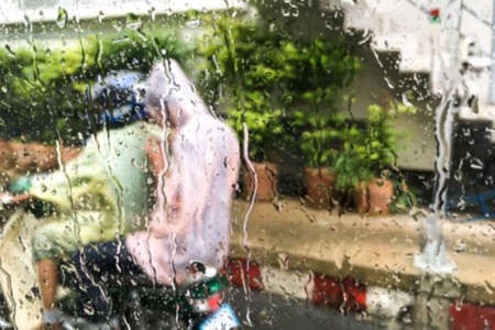 Blurred water drops on front mirror car and people wearing rain color clothes (rain suit) riding a motorbike (motorcycle) background- rainy day & abstract concept.の写真素材