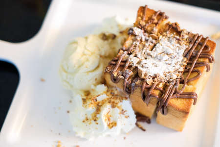 The toast bread topped with chocolate & almonds, whipped cream and vanilla ice cream serve on white dish for dessert background or texture.の写真素材