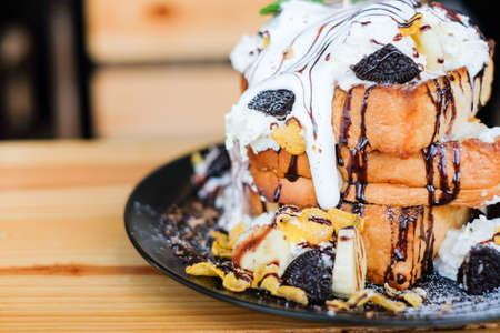 The triple toast bread topped with chocolate sauce, cereals, cookies, white cream, banana and vanilla ice cream serve on black dish for dessert background or texture.の写真素材