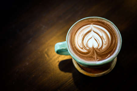 Homemade hot fresh cocoa with patterned white milk froth on surface in cup with wooden saucer (bottom plate) serve on wooden table, for beverage background - healthy diet concept.の写真素材