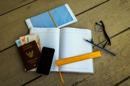 Thailand passport with money, pencil and yellow ruler for blank notebook (write your travel note), mobile phone and glasses - concept prepare to travel.の写真素材