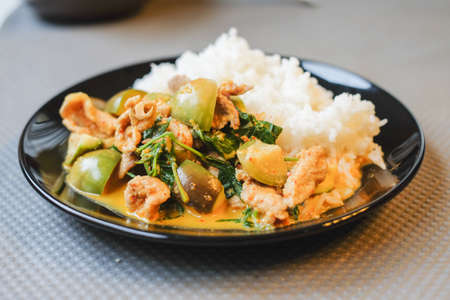 Green curry pork in coconut milk with eggplant and steamed rice serve on black plate.の写真素材