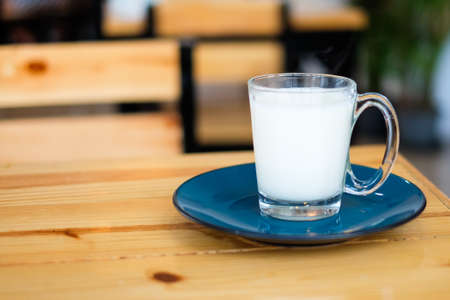 Homemade hot fresh milk in clear glass with blue saucer (bottom plate) serve on wooden table, for beverage background or texture - healthy diet concept.の写真素材