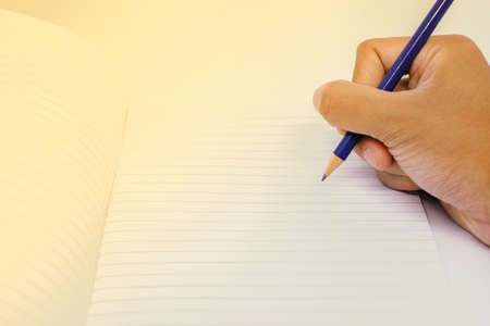 Hand with pencil writing on blank white notebook for background or texture.の写真素材