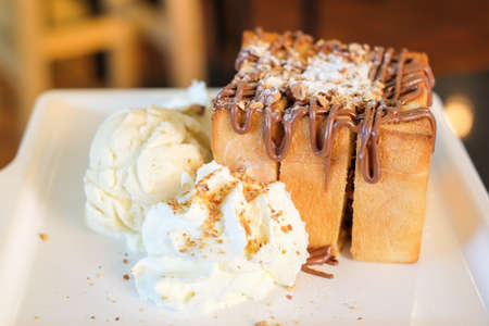 The toast bread topped with chocolate & almonds, whipped cream and vanilla ice cream serve on white dish for dessert background or texture.の写真素材