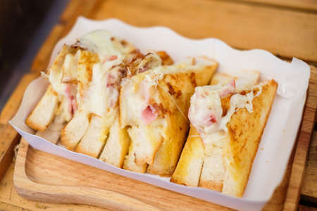Close up homemade "Bacon and Ham put on bread with cheddar & mozzarella cheese" serve on white paper box for food background or texture - breakfast concept.の写真素材