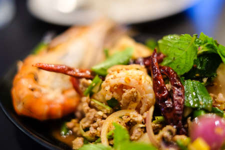 Big shrimps and squids and spicy minced pork mixed together with various herbs and vegetables including dried chilli served on black plate, for thai food background or texture.の写真素材
