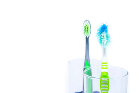 New toothbrush and old toothbrush (damaged) in clear glass for teeth cleaning isolated on white background - concept "How often should you change your toothbrush ? "の写真素材