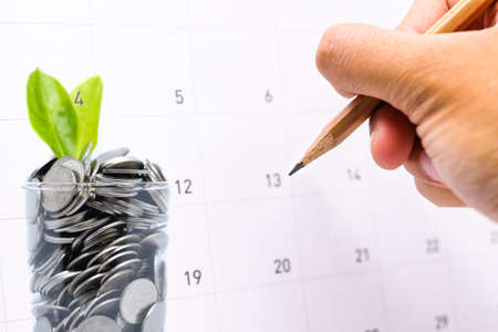 Plan to saving money in glass for your investment future is similar to growing green leaves on tree and write a message on calender for background or texture - economical & activity 2018 concept.の写真素材