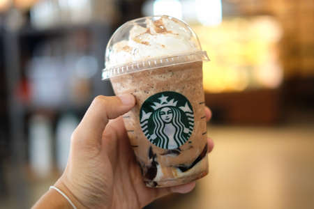 Bangkok, Thailand - January 30, 2018 :  Hand holding Ice Frappuccino (Cappuccino & Frappe) with blurred background & Starbucks coffee sign.のeditorial素材