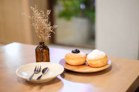 Blueberry Donut and Coconut Donut with powder serve on wooden plate with spoon and fork set on table with vintage flower in clear bottle - Homemade Bakery & Dessert concept.の写真素材
