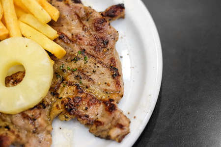 Grilled kurobuta pork (breed of pig originating from English of Berkshire) with black pepper sauce, pineapple and french fries serve on white plate - food concept.の写真素材