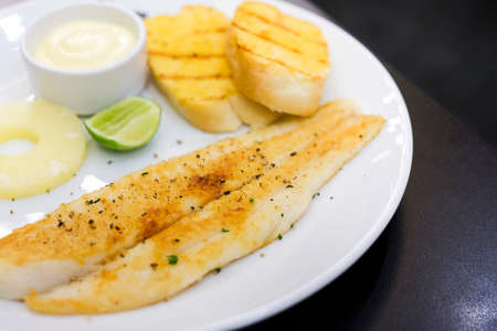 Grilled dolly fish with black pepper, mayonnaise sauce, lemon, pineapple and garlic bread recipe serve on white plate - food concept.の写真素材