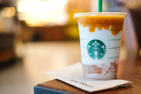 Bangkok, Thailand - August 23, 2018 : "Apricot and peach yogurt frappuccino " with whipped cream on brown table & Starbucks coffee sign.のeditorial素材