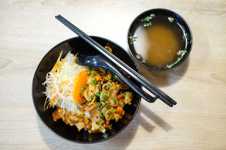 Rice with grilled pork teriyaki and spring onion on top in the black plastic bowl with soup for japanese food background or texture.の写真素材