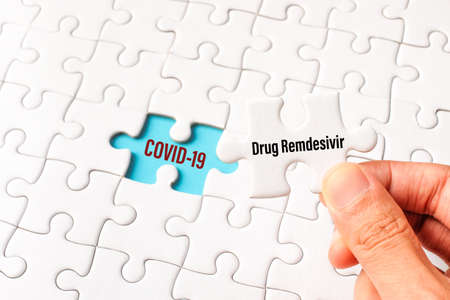 The drug remdesivir word on white jigsaw puzzle go to replace COVID-19 word on blue gap - idea answer concept.の写真素材