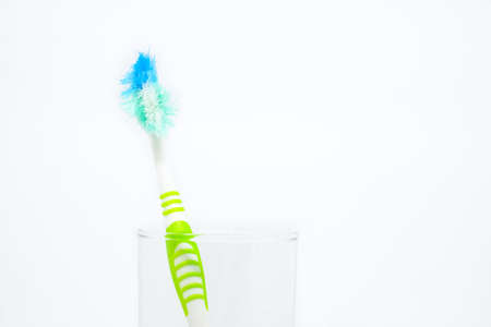 Old toothbrush (damaged) in clear glass for teeth cleaning isolated on white background - concept "How often should you change your toothbrush ? "の写真素材