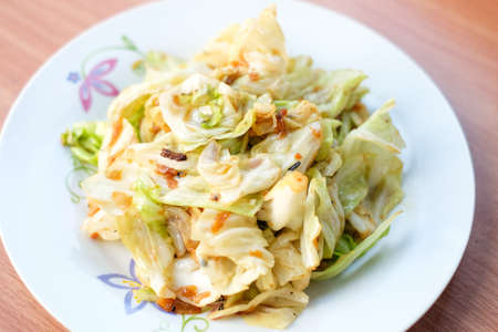 The closeup hot stir fried cabbage with fish sauce serve on white dish set on brown table - homemade food concept.の写真素材