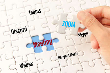 Bangkok, Thailand - May 10, 2020 : Hand holding zoom word on white jigsaw puzzle is connect to meeting word on blue gap - idea match (Teams, Discord, webex, Hangout Meets, skype) concept.Bangkok, Thailand - May 10, 2020 : Hand holding zoom word on white jのeditorial素材