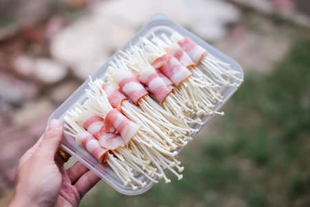 Hand holding a golden needle mushroom wrapped in bacon - homemade food concept.の写真素材