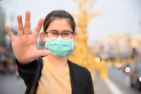 Woman wearing surgical mask for protect virus and show stop hand gesture for social distancing (focus at her hand). Social distancing is the physical space between people to avoid spreading illness.の写真素材