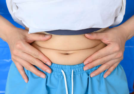 Close up of Woman touching her fat belly, woman's hand holding excessive belly fat. Being overweight is one of the leading causes of major diseases such as heart disease, stroke, high blood pressure.の写真素材