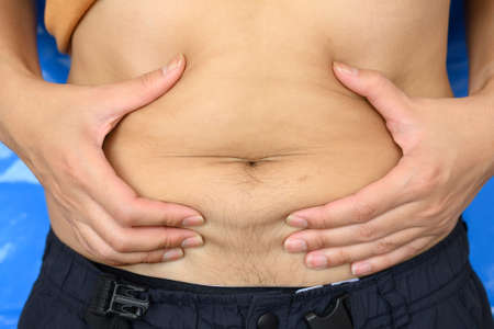 Close up of Man touching his fat belly, Men's hand holding excessive belly fat. Being overweight is one of the leading causes of major diseases such as heart disease, stroke, high blood pressure.の写真素材