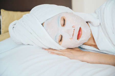 Portrait of young woman sleeping on bed while applying facial mask on her face. Conceptual of young woman lifestyle in her private room.の写真素材