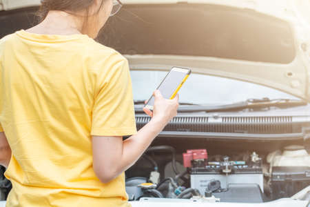 Back view of young woman trying to call someone to help her after her car breakdown on the road. Conceptual of car accident on the roadの写真素材