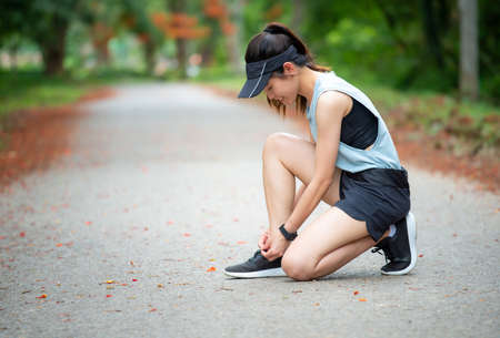 Portrait of young runner woman knee down on the road for tying shoelaces. Conceptual of woman getting ready for jogging in the park.の写真素材