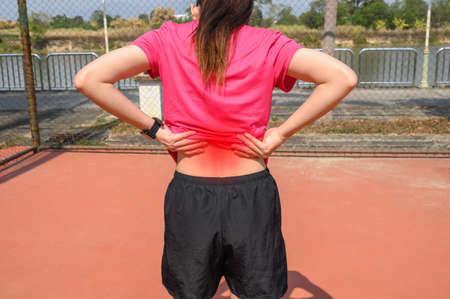 Back view of young runner woman suffering from lower back pain or sore waist after running or sport...