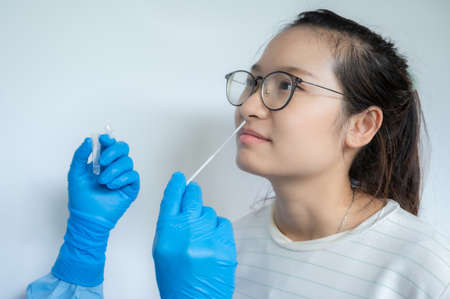 Close up of doctor hands trying to taking a nasal swab from Asian woman for testing diagnosis of covid-19 infection. A nasal swab is a test that takes a sample of cells from the nasopharynx.の写真素材