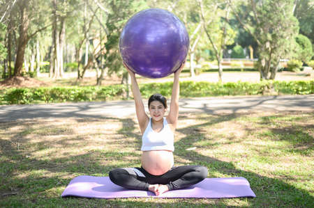 Portrait of young pregnant woman doing Prenatal Yoga with fit ball in the park. Prenatal yoga is a way to maintain a healthy mind and body to increase strength and flexibility.の写真素材