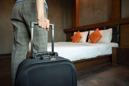 Cropped shot of tourist woman  pulling her luggage in hotel bedroom after check-in. Sharp focus at her hand.の写真素材