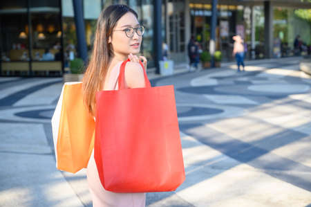 Portrait of young Asian woman holding shopping bags after shopping in retail store. Shot of Consumerism and Shopping concept.の写真素材