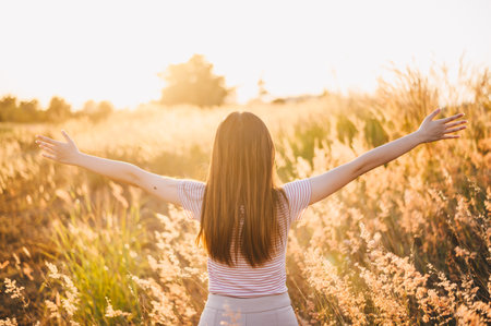 Back view of active woman raised her hands, feeling freedom in meadow grass field with warm sunshine. Conceptual of happiness woman enjoying her life.の写真素材