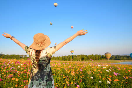Back view of young tourist woman visiting cosmos flowers field and looking to hot air balloons festival in Chiang Rai province of Thailand.の写真素材