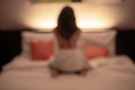 Abstract of blurred background image (defocus) of Prostitution woman sitting on the bed in hotel...