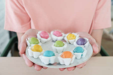 Cropped shot view of woman holding Thai dessert named Khanom Sai Sai a palm sugar sweetened ball is...