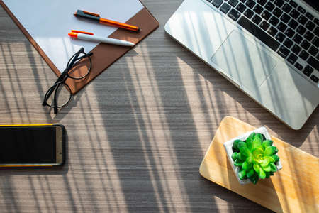 Top view of office table desk with notebook computer, mobile phone, paper, pencil, eyeglasses and...