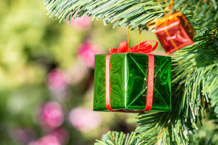 Close up of a wrapped gift box hanging on a branch of Christmas tree. Gift or present is an item given to someone without the expectation of payment or anything in return.の写真素材