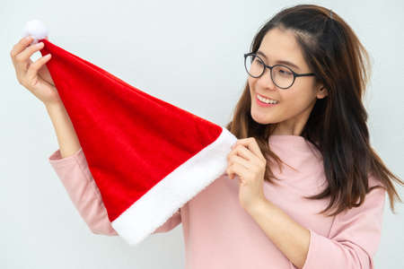 Portrait of happiness Asian woman holding Santa hat and lean on the white wall background. Celebration of Christmas and New year festival concepts.の写真素材