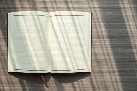 Top view of open notebook on wood table with blank pages, natural light and shadow reflection across...