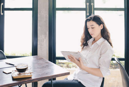 Portrait of concentrated young beautiful businesswoman working on tablet and waiting for her customer in cafe. Conceptual of businesswoman lifestyle.の写真素材