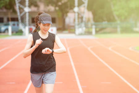 Portrait of young athlete runner woman running in the running track and she looking to her smart watch. Running track is a rubberized artificial running surface for track and field athletics.の写真素材