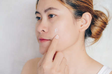 Close-up of young Asian woman applying moisturizer cream on her face. Conceptual of beauty and skin care.の写真素材