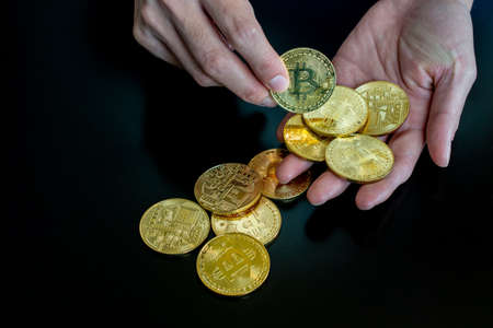 Close up of someone hand holding golden Bitcoin on black table background. Bitcoin is one of the...